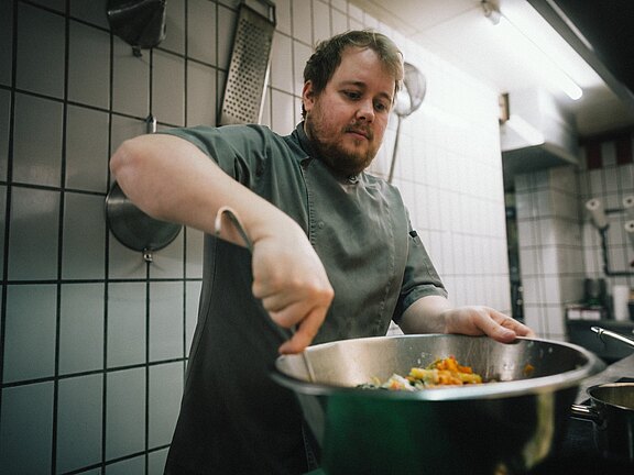 Koch im Vitalhotel Simon bereitet mit frischen Zutaten ein Gericht in der Hotelküche zu.