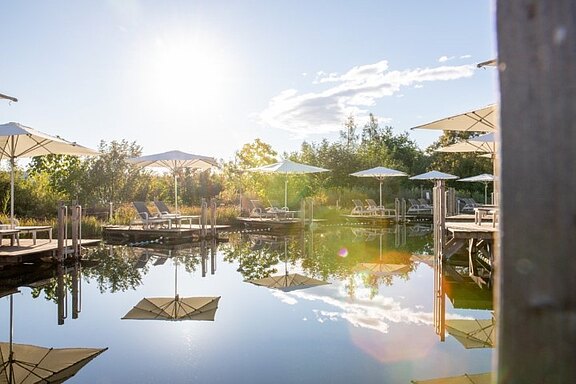 Sonnenuntergang am Naturbadeteich der AVITA Therme mit romantischen Stegen, Liegen und Sonnenschirmen.