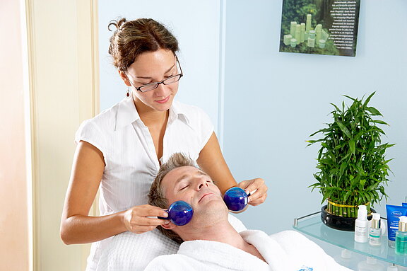 Wohltuende Gesichtsbehandlung für nachhaltige Entspannung im Spa des Vitalhotels Simon. Mann entspannt bei einer Gesichtsbehandlung mit Kügelchen im Spa-Bereich des Vitalhotels Simon.